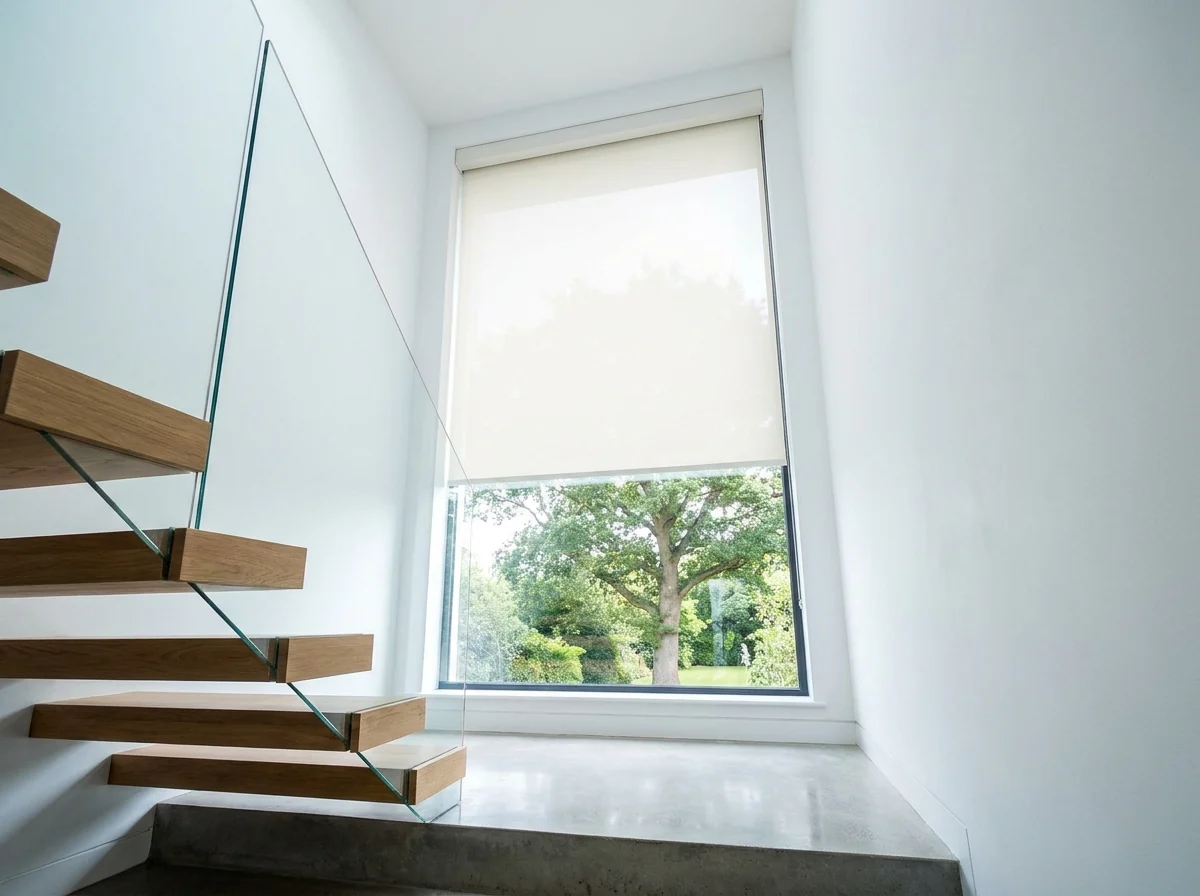 Motorised off-white roller blind on a four-metre stairwell window in a Constantia home, floating oak treads and a glass balustrade alongside